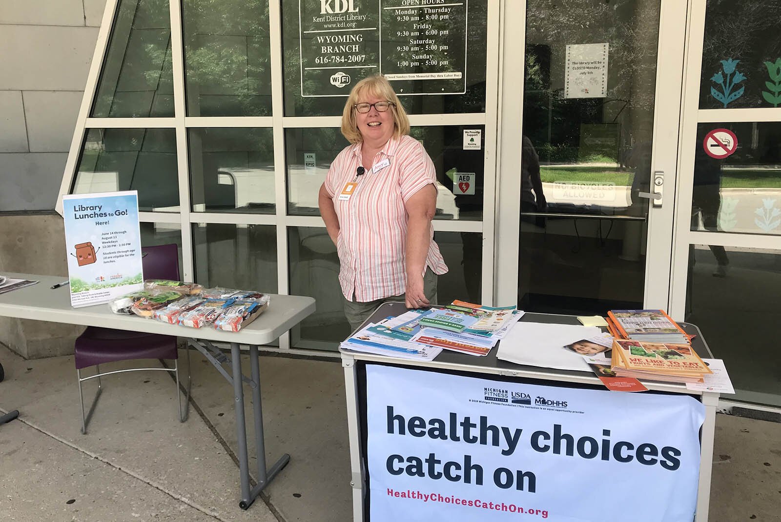 KISD Nutrition Educator Amy Klinkoski promotes the Kentwood Farmers Market during a summertime lunch pickup at the Kent District Library's Wyoming branch.