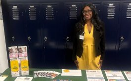LaShawnda Bates, wearing a yellow dress, stands in front of a table with health brochures on it.