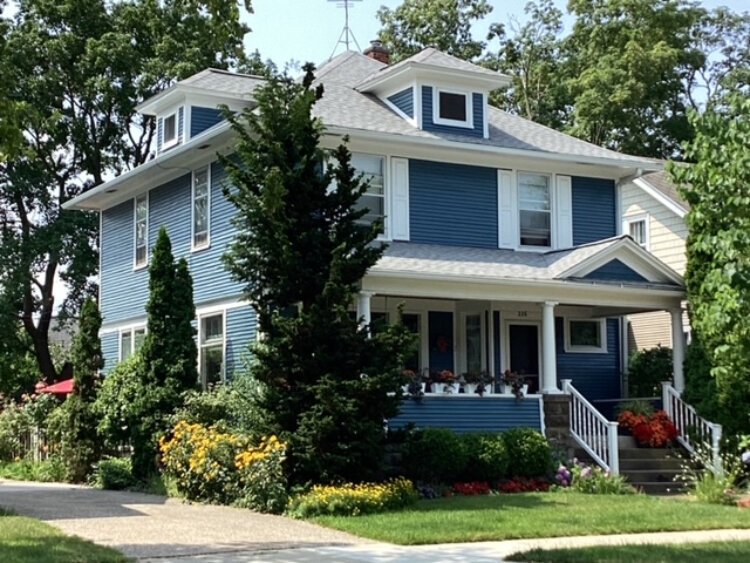 Pictured is a lovingly preserved American Foursquare home with kitchen, living room, dining room, and possibly a parlor or den downstairs, and four bedrooms upstairs. The porch connects the home to the neighborhood.